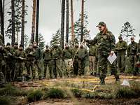 Eine norwegische Soldatin steht in einem Geländesandkasten und hat einen Stock in der Hand. Im Hintergrund viele Soldaten. 