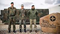 Drei Soldaten stehen zum gemeinsamen Gruppenbild vor dem Eingangsstein des deutschen Camps im litauischen Pabrade 