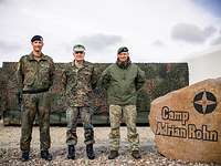 Drei Soldaten stehen zum gemeinsamen Gruppenbild vor dem Eingangsstein des deutschen Camps im litauischen Pabrade 