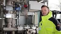 A man wearing a bright yellow jacket, standing in front of a technical plant installed in a container.