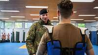 Zwei Soldaten stehen sich in einer Sporthalle gegenüber und sprechen miteinander. Der eine trägt eine Nahkampfausrüstung.