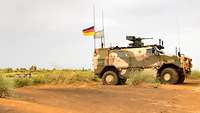 Ein geschütztes Fahrzeug der Bundeswehr in Wüstentarn mit einer Deutschlandflagge und einer Flagge der Vereinten Nationen