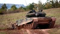 Ein Panzer in schneller Zufahrt, die Ketten schleudern Dreck in die Luft.