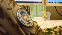 An einem Schreibtisch sitzt ein Soldat mit einer Tastatur und zwei Monitoren. Davor ein Papierengel und eine Grußkarte.