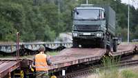 Ein Lkw der Bundeswehr fährt auf einen Bahnwaggon auf. Soldat im Vordergrund weist ein.