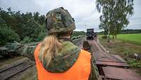 Einweiserin Soldatin mit Helm und Warnweste weist Lkw zum Auffahren auf den Waggon ein