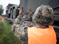 Millimeterarbeit Soldat mit Helm und Warnweste steht neben Waggon und weist Lkw per Handzeichen ein