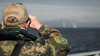 Ein Soldat beobachtet durch ein Fernglas die Artillerieeinschläge auf dem Meer