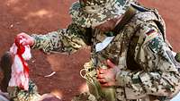 Ein Soldat kniet neben dem Bein eines anderen Soldaten mit blutverschmierten Händen und einem Tuch in der Hand