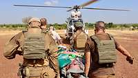Vier Personen tragen einen Verletzten zu einem Helikopter