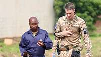 Ein deutscher Soldat und ein malischer Mann im Blaumann laufen nebeneinander und unterhalten sich 