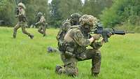 Zwei Soldaten sind kniend mit dem Gewehr im Anschlag. Dahinter laufen Soldaten.