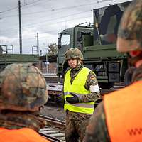 Ein Soldat gestikuliert vor anderen Soldaten im Bahn und Gleisbereich.