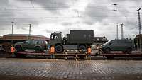Auf einem Eisenbahnwaggon stehen Militärfahrzeuge und Soldaten arbeiten daran.