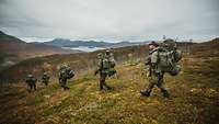 Soldaten marschieren mit Gepäck im freien Gelände einen Berg hinunter