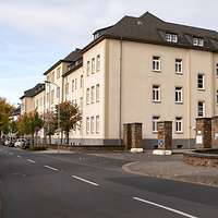 Ein sandsteinfarbenes Gebäude umringt von herbstlichen Bäumen.