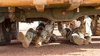 Zwei Soldaten liegen unter einem Fahrzeug und prüfen den Unterboden
