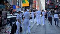 Personen in weißer Marineuniform stehen in einer Gruppe auf einem Platz zwischen Hochhäusern.
