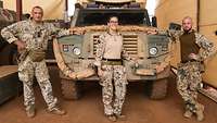 Eine Soldatin und zwei Soldaten in sandfarbenen Tarnuniformen stehen vor einem Eagle mit Blaulicht 