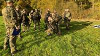 Mehrere Soldaten stehen zur Ausbildung um zwei Kameraden, die einen Verband anlegen.