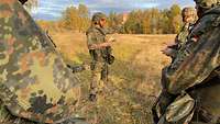 Ein Offizier steht im Gefechtsanzug im Gelände und weist Soldaten ein.