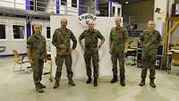 Fünf Soldaten stehen nebeneinander für ein Gruppenfoto vor einer weißen Wand.