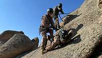 Drei Soldaten hängen an Seilen gesichert an einem Felsen.