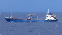 Der Sea Lynx schwebt über dem Handelsschiff. Ein Soldat seilt sich per Fast Rope-Verfahren auf das Handelsschiff ab.