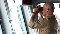 Der Kommandant steht mit einem Fernglas auf der Brücke der „Bonn“