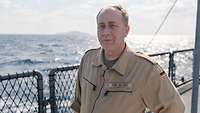 Ein Soldat steht an Oberdeck eines Schiffes. Im Hintergrund ist das Meer.