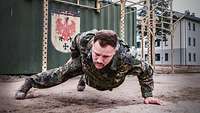 Ein Soldat macht einarmigen Liegestütz im Feldzug mit Schutzweste 