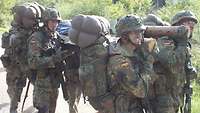 Vier Soldaten tragen eine Behelfstrage mit Soldat und Gepäck auf ihren Schultern.