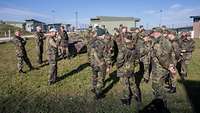 Eine Menschengruppe in Uniform steht in einem Bundeswehrlager auf einer grünen Wiese.