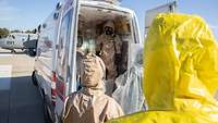 Ankunft am Rettungswagen Der verpackte Pilot wird von Rettungskräften, ebenfalls in Schutzanzügen und -masken, am Wagen in Empfang genommen