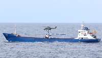 Hubschrauber im Anflug Ein Handelsschiff befindet sich auf dem Wasser. Über dem Schiff fliegt ein Helikopter, ein Soldat seilt sich ab.