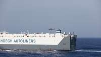 Ein Hubschrauber fliegt über einem Schiff. Der ECLO seilt sich per Fast-Roping auf ein Handelsschiff ab.