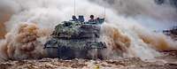 Ein Panzer vom Typ Leopard 2 A6 fährt im Gelände und wirbelt viel Staub auf