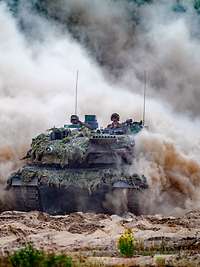 Ein Panzer vom Typ Leopard 2 A6 fährt im Gelände und wirbelt viel Staub auf