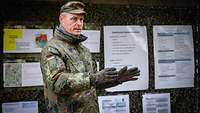 Ein Soldat steht vor einer Wand mit laminierten Blättern angebracht. Er spricht.