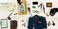 Auf einem Tisch liegen diverse Gegenstände, zum Beispiel eine Landkarte, Uniform, eine Trainerkappe, Ei oder ein Anker