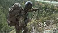 An einer schroffen Bergwand legt ein Soldat ein Seil als Handlauf aus. 