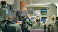 Vor dem Flug kommt der Simulator Vier Schüler sitzen vor einem großen technischen Schaltpult, ein Soldat spricht mit ihnen.