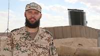 Ein Soldat steht in einem Bundeswehrcamp vor Sandsäcken und einer Radaranlage
