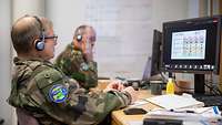 Two soldiers sit next to each other at a table and look at the screens of their PCs