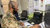 Ein Soldat sitzt am Computer und telefoniert über das Headset