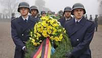 Mehrere Soldaten in blauer Uniform und mit Helm tragen Trauer-Kränze.