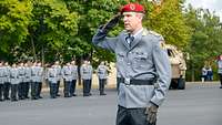 Ein Offizier meldet mit militärischem Gruß, dahinter angetretene Soldaten in Formation.