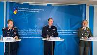 Drei Soldaten vor Leinwand mit NATO-Symbol
