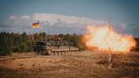 Ein Kampfpanzer schießt scharf im Gelände. Ein Feuerball strömt aus dem Rohr.