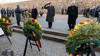 Drei Personen stehen nebeneinander vor einem Ehrenmal auf einem Festungsplatz. Um sie rum stehen viele Menschen.